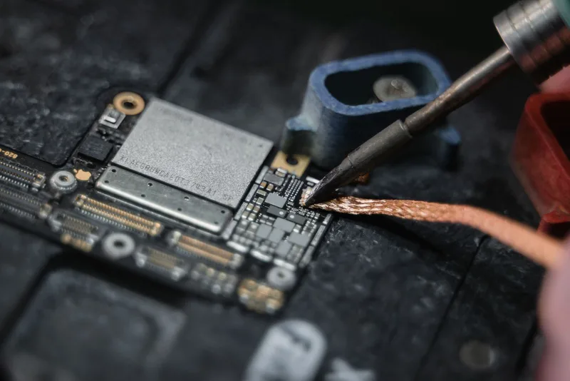 Primer plano de un cautín soldando un cable sobre una placa de circuito impreso